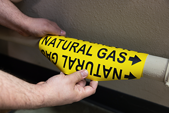 A "natural gas" pipe label being securely placed on a pipe.